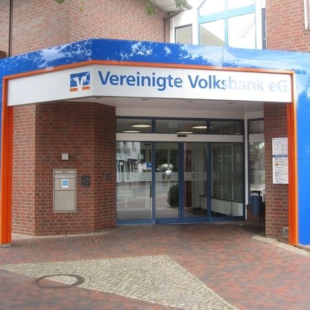 Eingang der Vereinigten Volksbank eG mit blau-orangem Vordach, Glastüren und Backsteinmauern